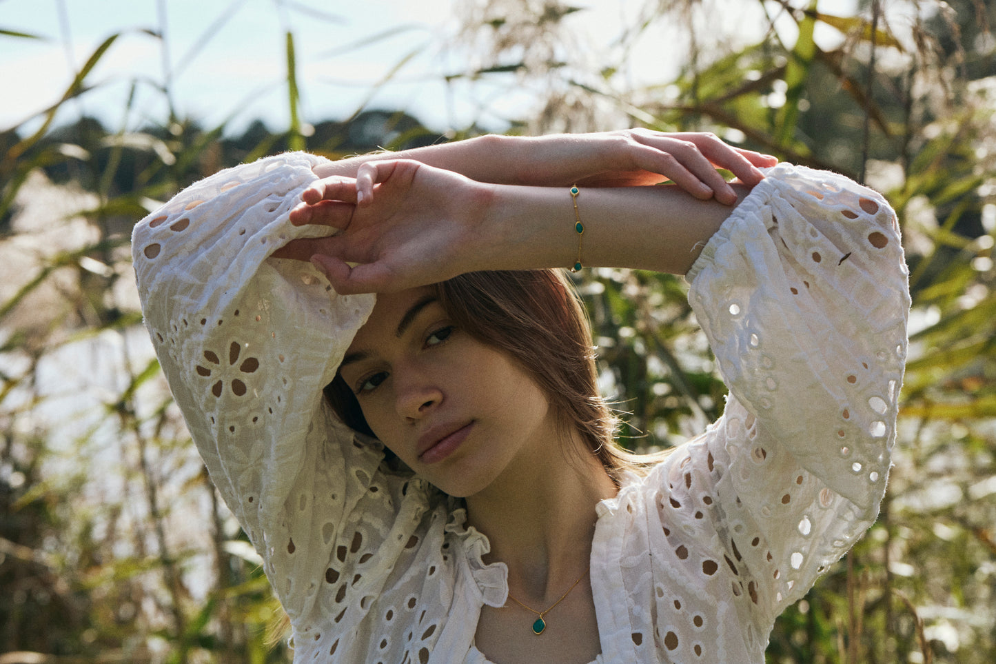 Woman wearing amazonite necklace and bracelet in a white lace top in a natural setting