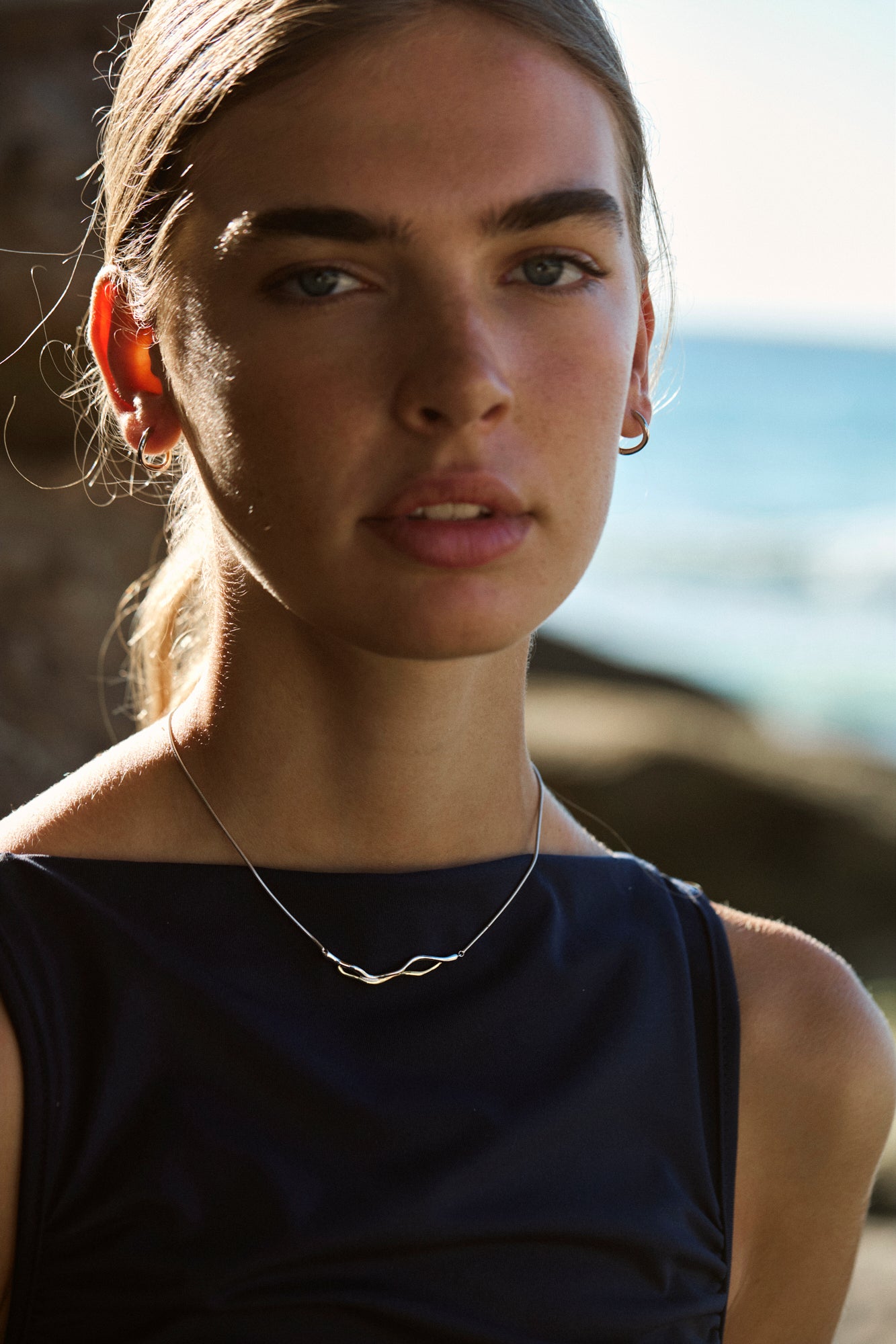 Woman with a wave-like necklace against a blurred natural background