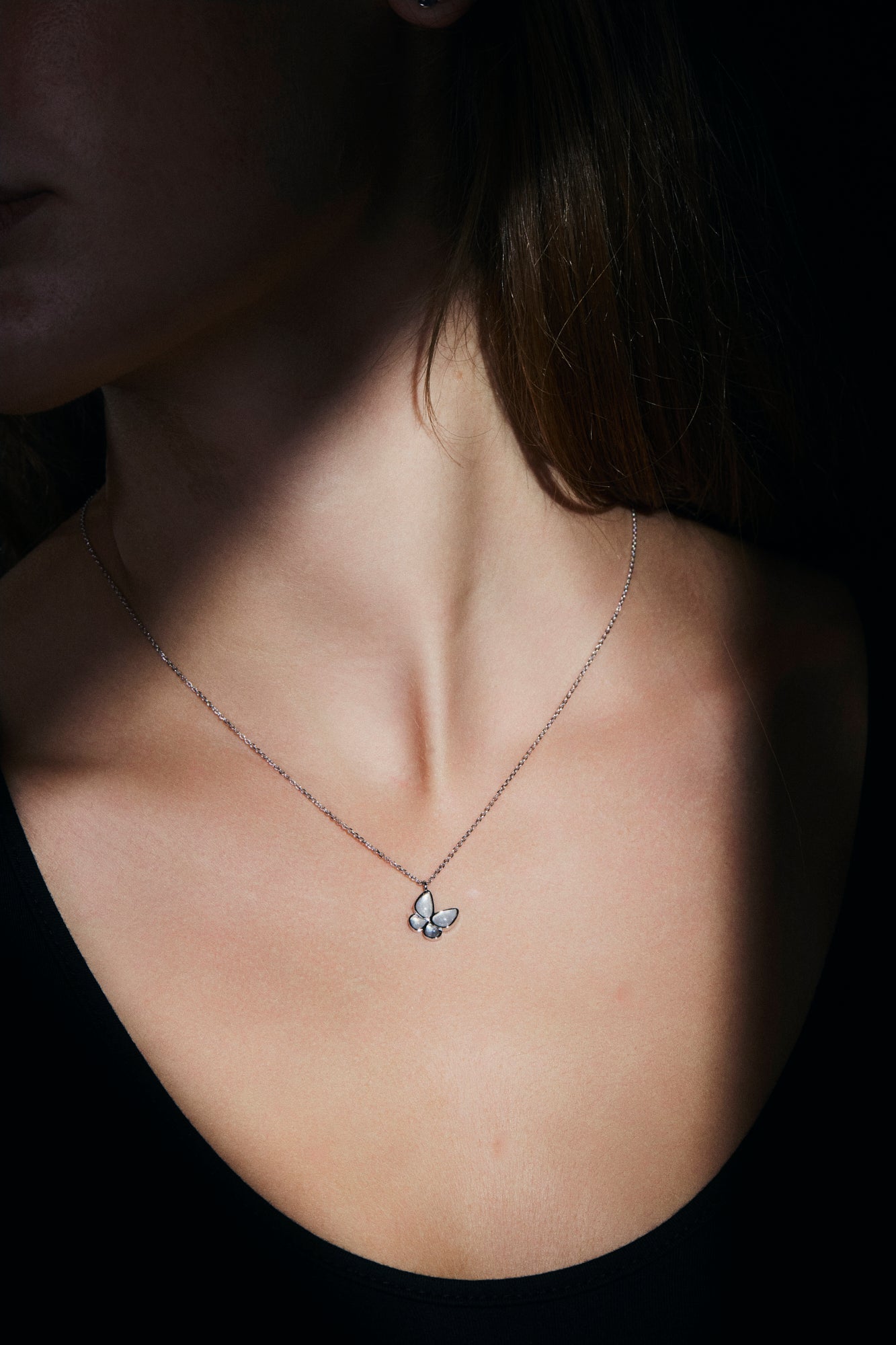 Necklace with a small butterfly silver pendant worn by a person against a dark background